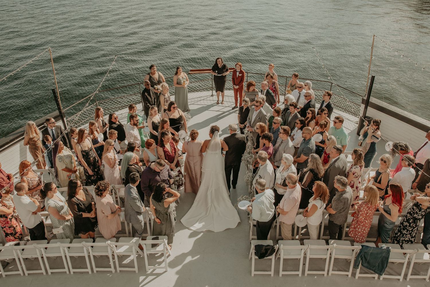 Wedding guests gather on a dock by the water during a sunset ceremony in a series of panoramic shots.