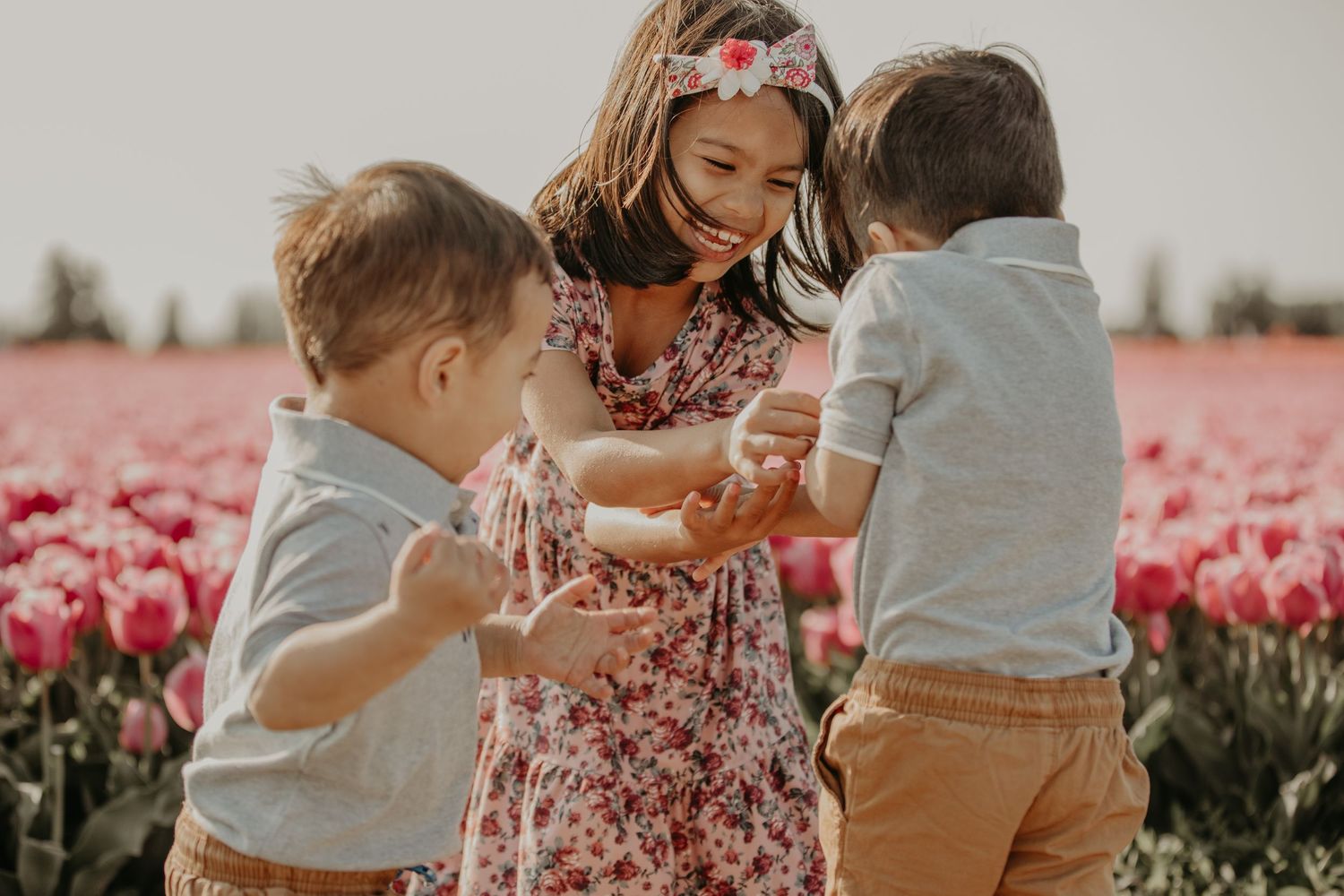 Children gather together among rows of pink tulips on a bright spring day.