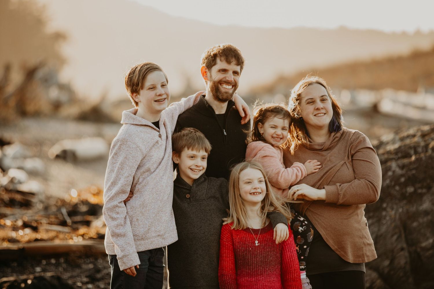 A family stands together at sunset on a rocky coastline in warm golden lighting.