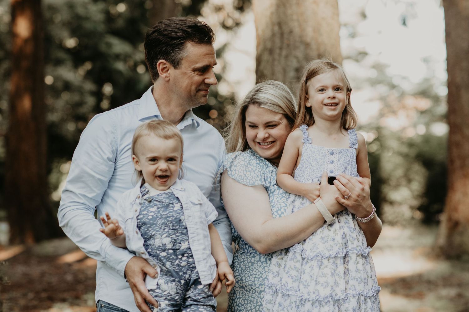 A heartwarming family portrait captured outdoors in a forest setting with soft natural lighting and joyful expressions.