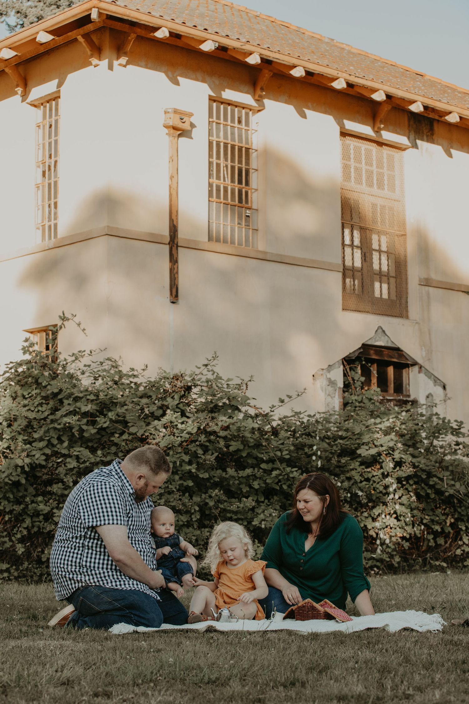 Family enjoying a sunset picnic on the lawn in front of a Spanish-style building with white stucco walls and wooden details.