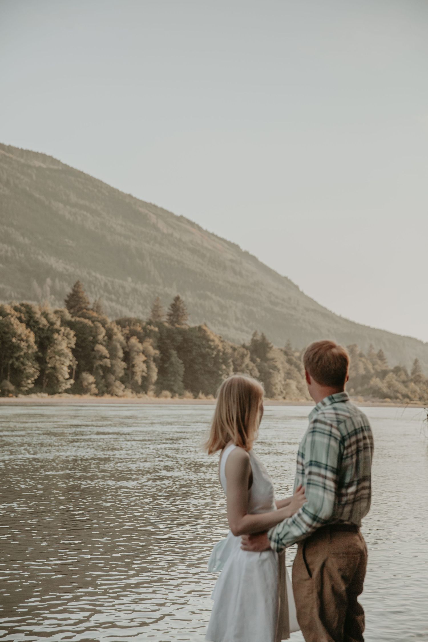 Romantic couple enjoying a peaceful moment by a serene lake surrounded by mountains in muted tones.