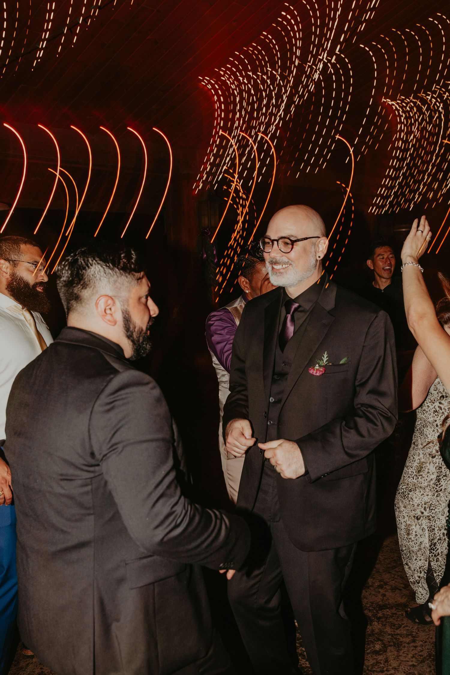 People dancing and celebrating at a dimly lit indoor reception with string lights overhead.