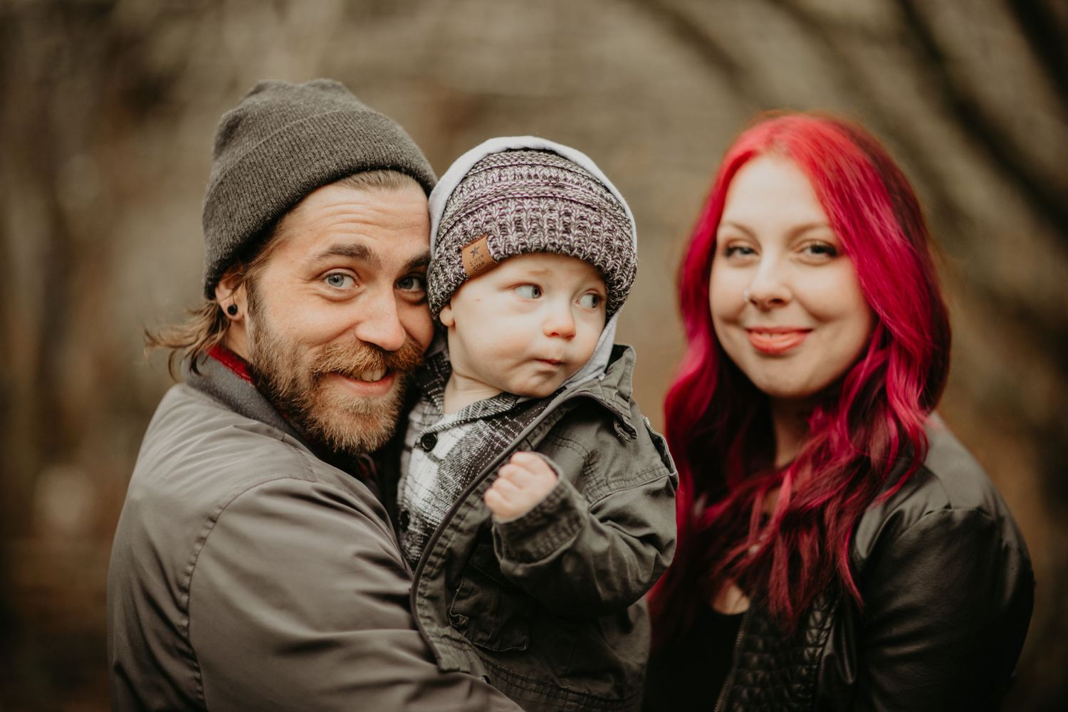 Family portrait outdoors in winter showing parents with young child against blurred natural background.