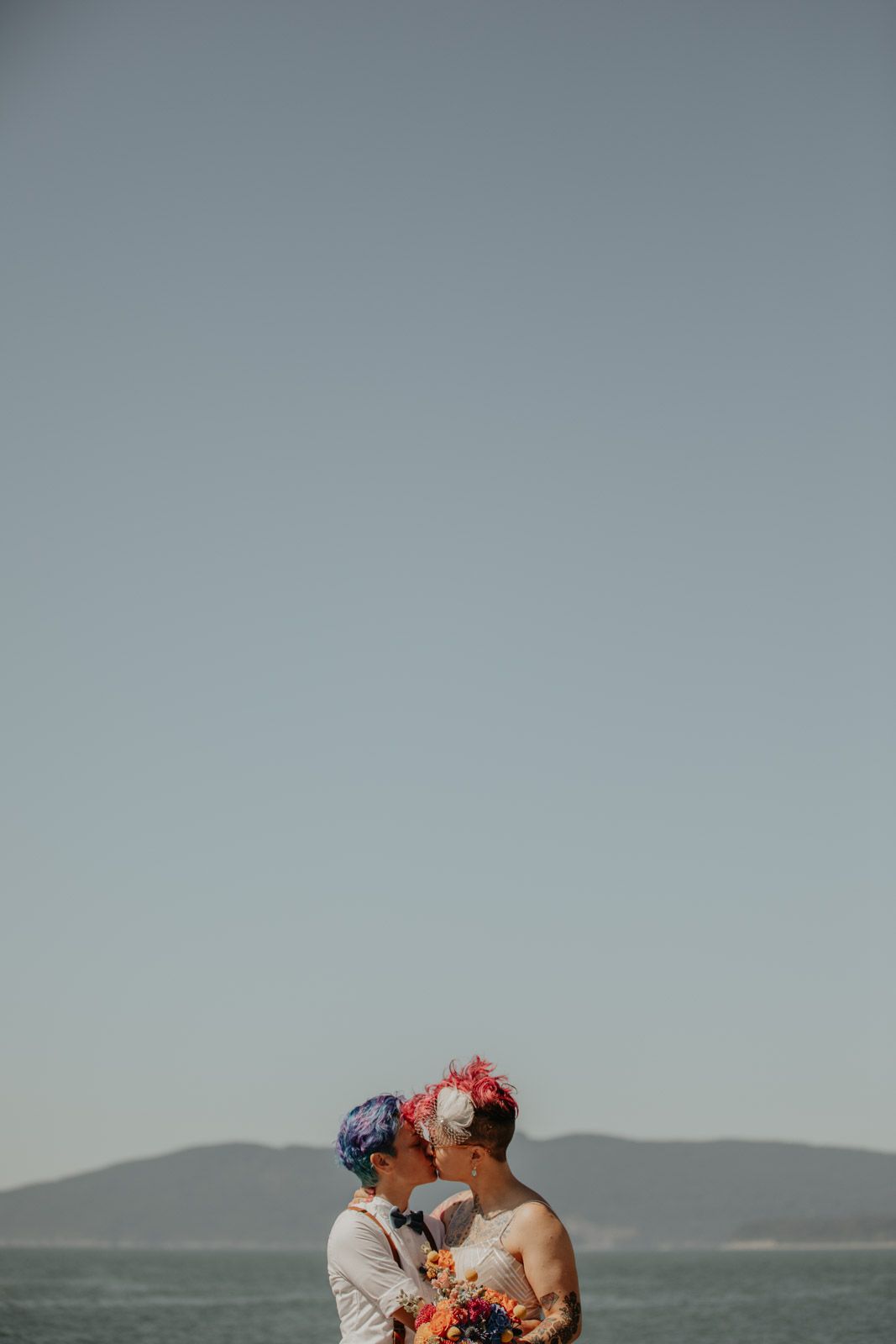 A couple sharing an intimate moment on a beach with mountains visible in the background.