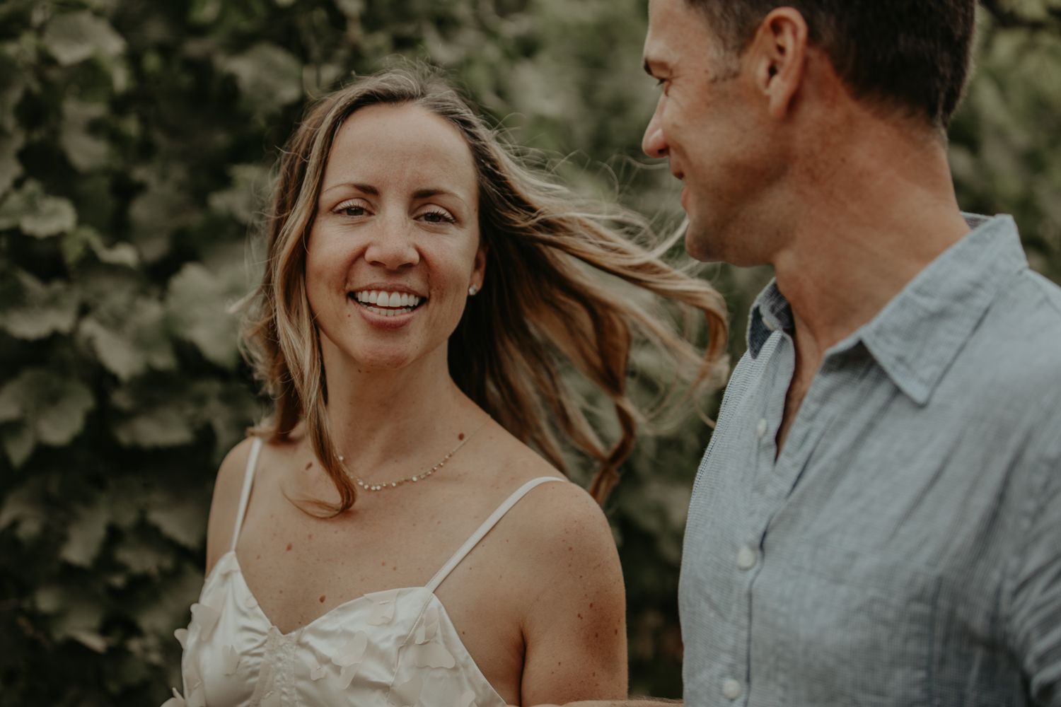 A couple shares intimate moments in an outdoor garden setting wearing gray and white attire.