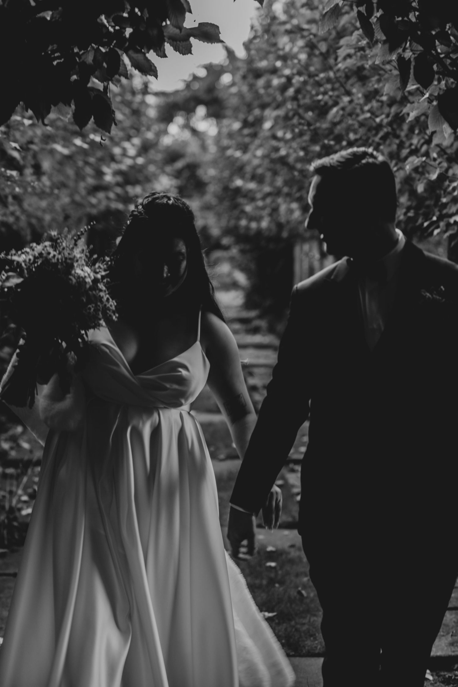 A newlywed couple walks hand in hand down a garden path on their wedding day.