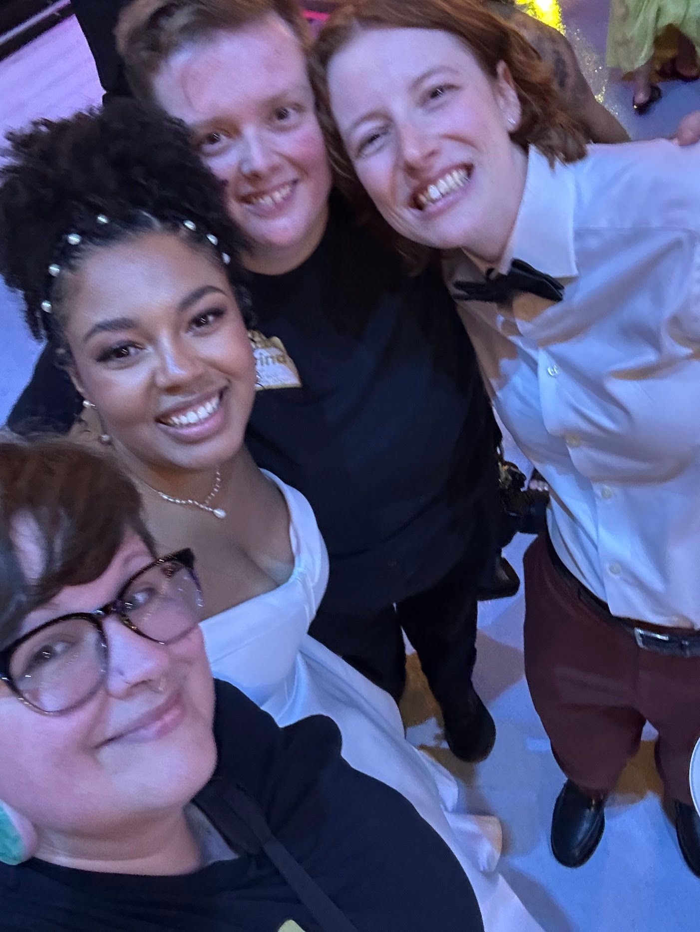 A group of friends smiling together in a casual setting with a purple-tinted lighting effect.