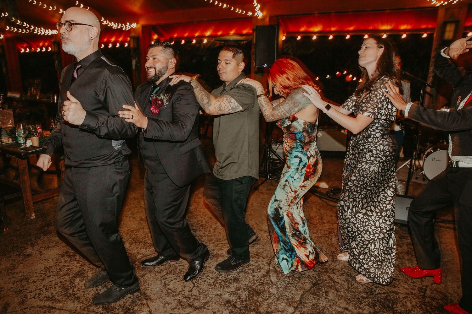 People dancing in a line at a festive event with string lights overhead.