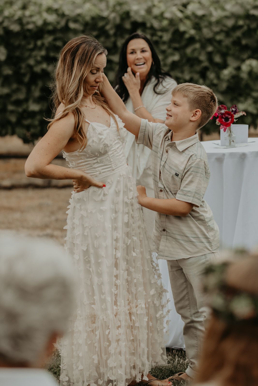 Candid moment at outdoor wedding reception with guests in white dress and casual attire sharing joyful laughter.