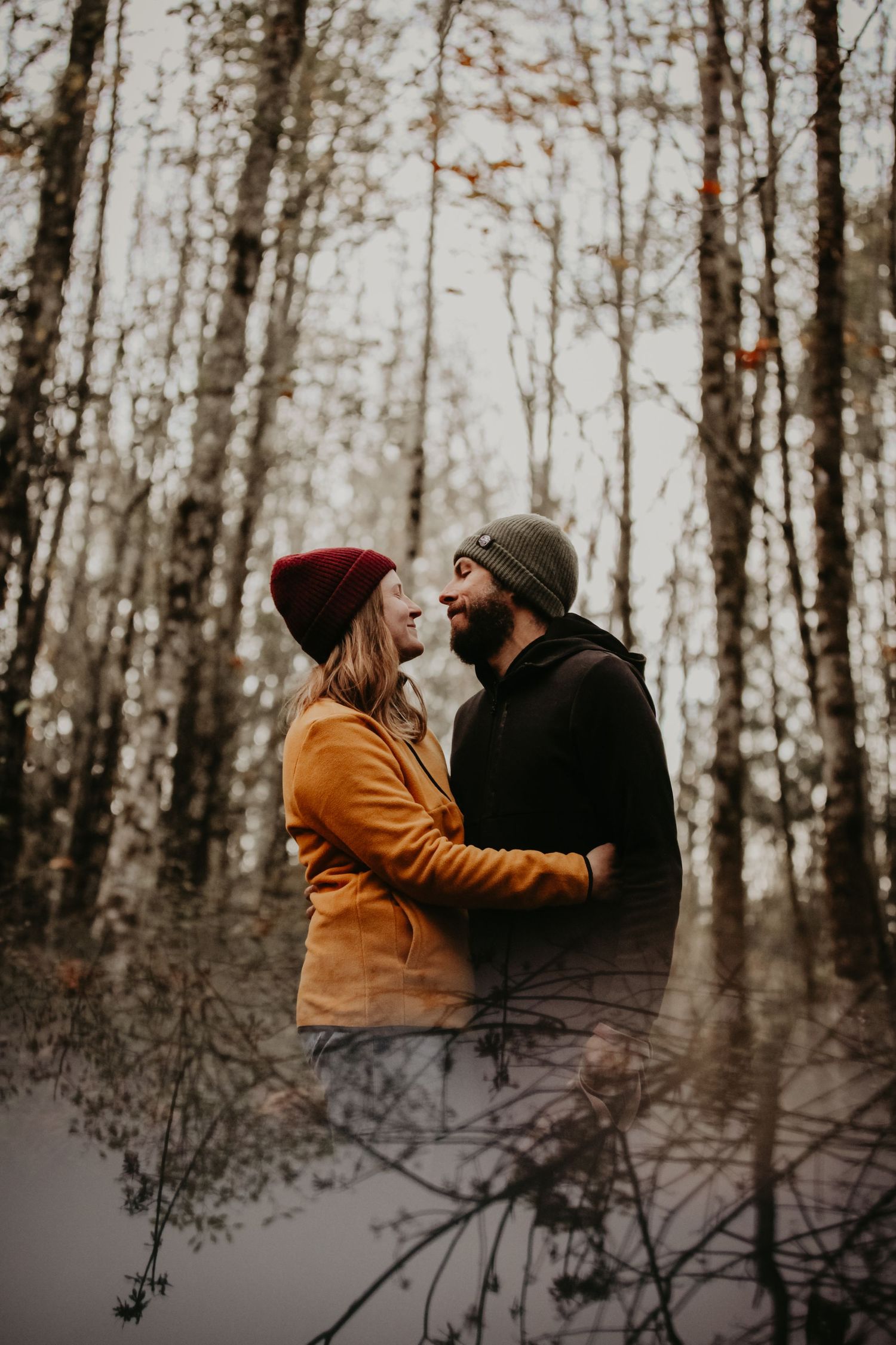 A couple in winter attire sharing an intimate moment in a misty forest with bare trees in the background.