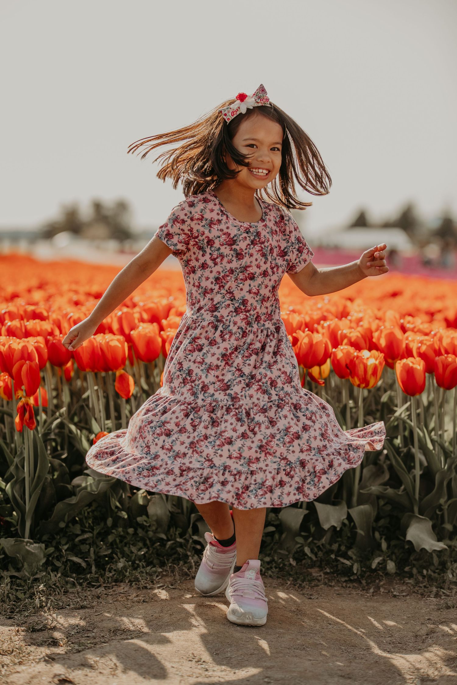 A person twirls in a floral dress among vibrant orange tulips, with their hair flowing in the breeze.