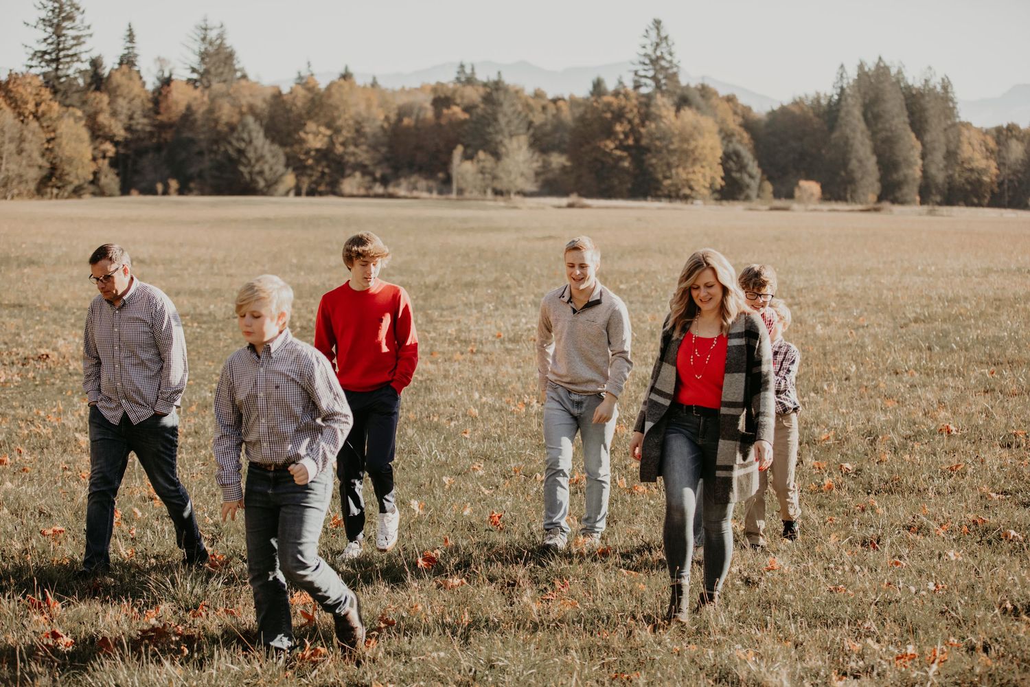 People enjoying a casual stroll together through a golden autumn field with evergreen trees in the background.