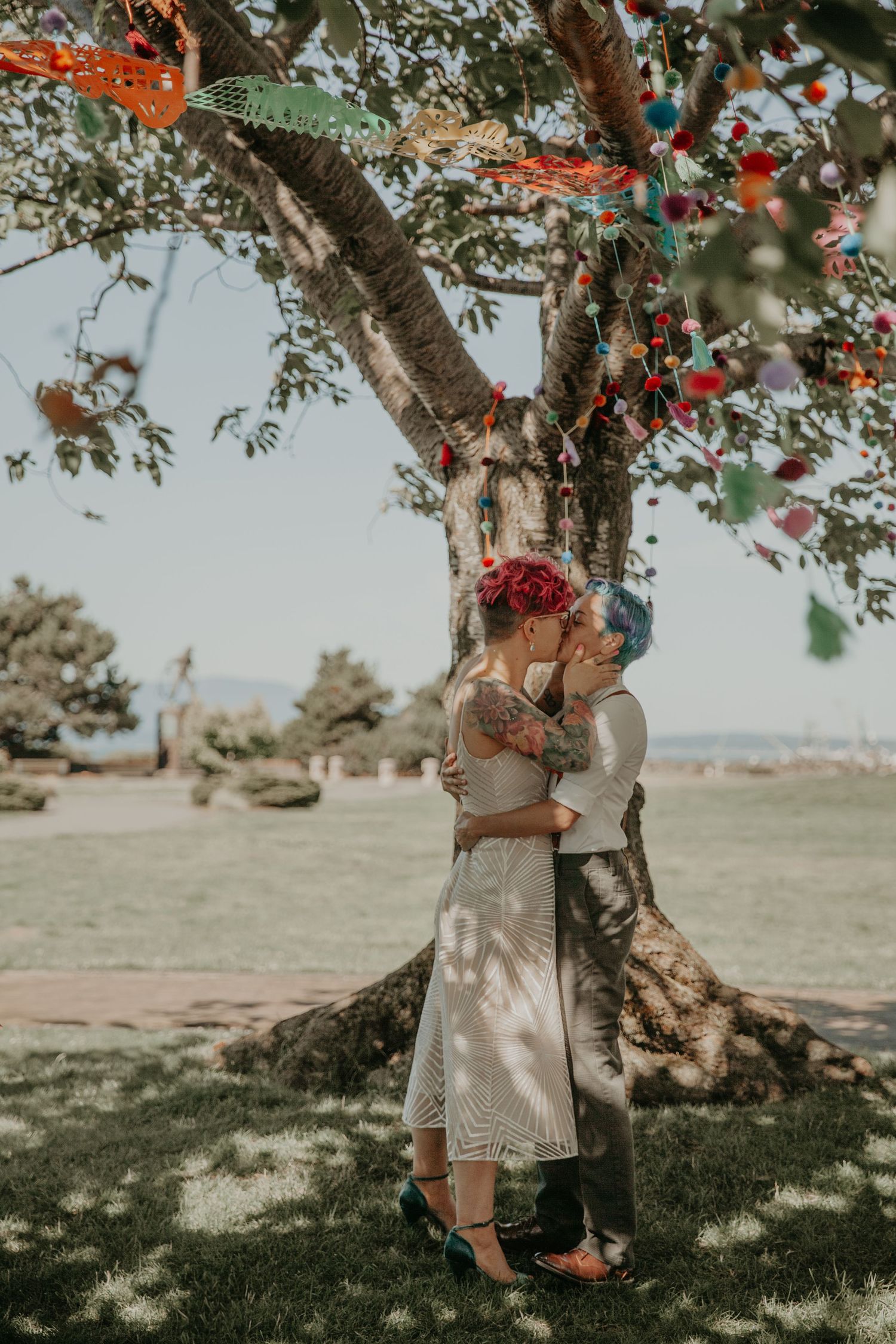 Romantic couple embraces under a blooming tree with orange and pink flowers in a dreamy outdoor setting.