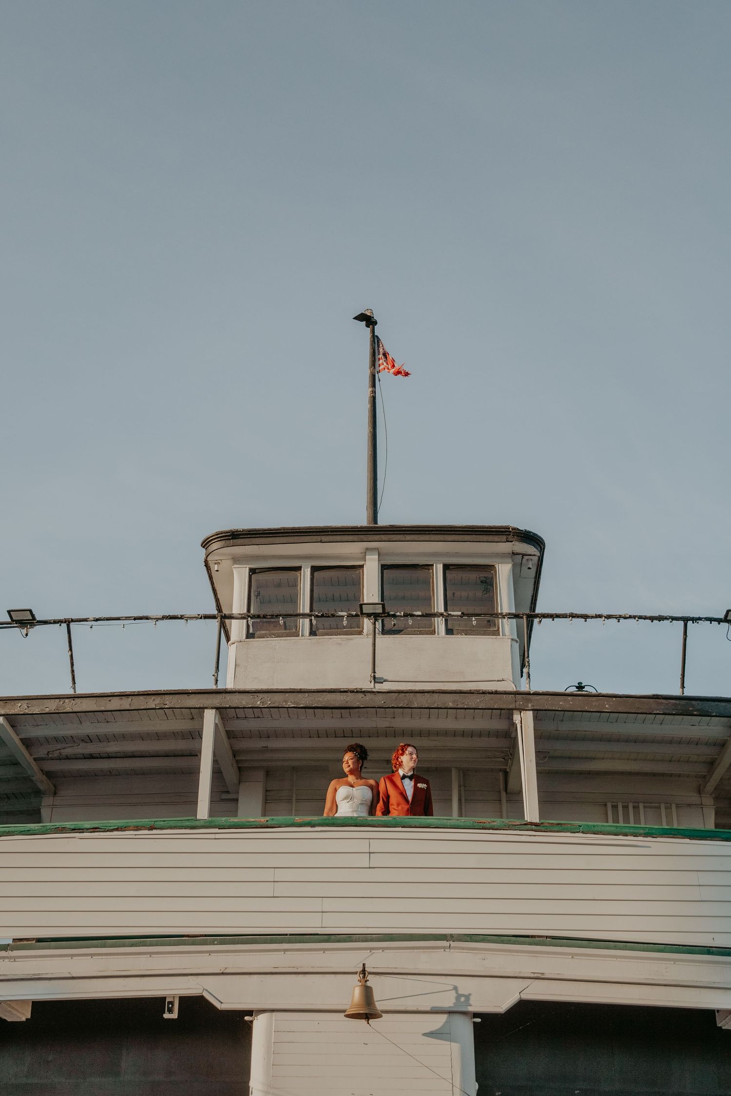 White boat deck with a small flag pole and railing against an overcast sky.