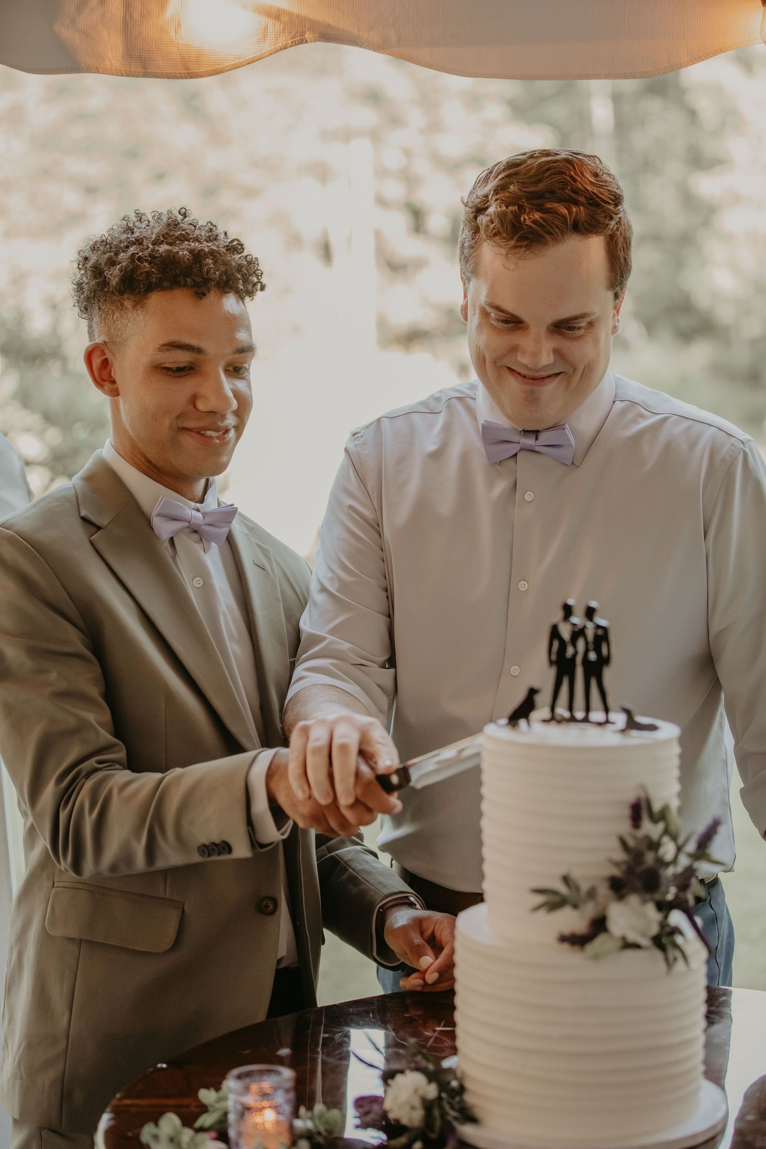 Two people in formal attire cutting into an elegant white wedding cake with delicate floral decorations.