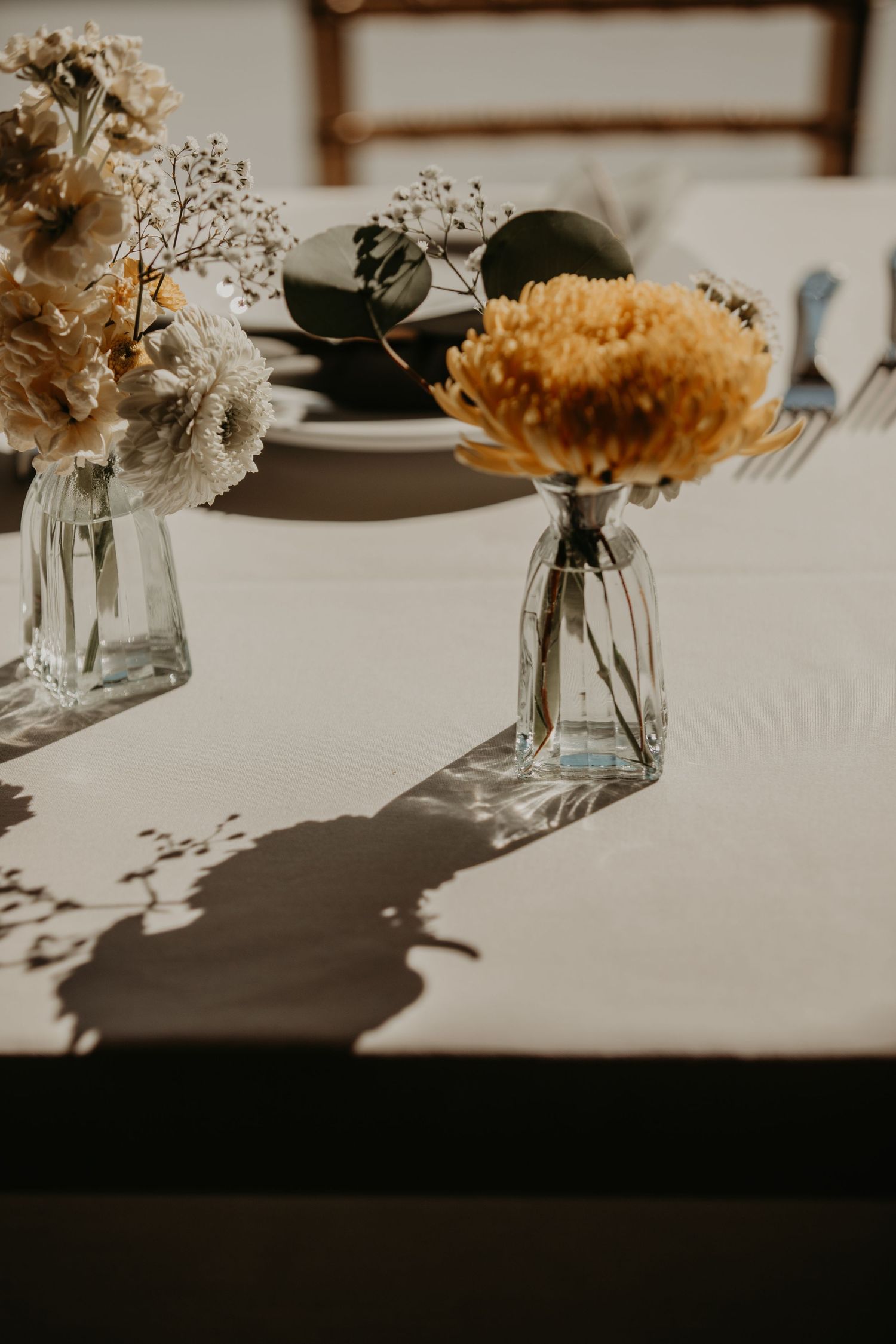 Delicate dried flowers arranged in clear glass vases on a white tablecloth.