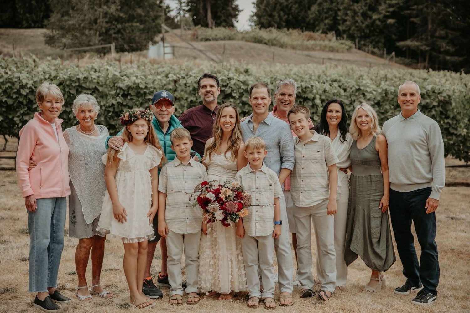 A large wedding party poses together outdoors in coordinated neutral-colored attire against a natural landscape backdrop.