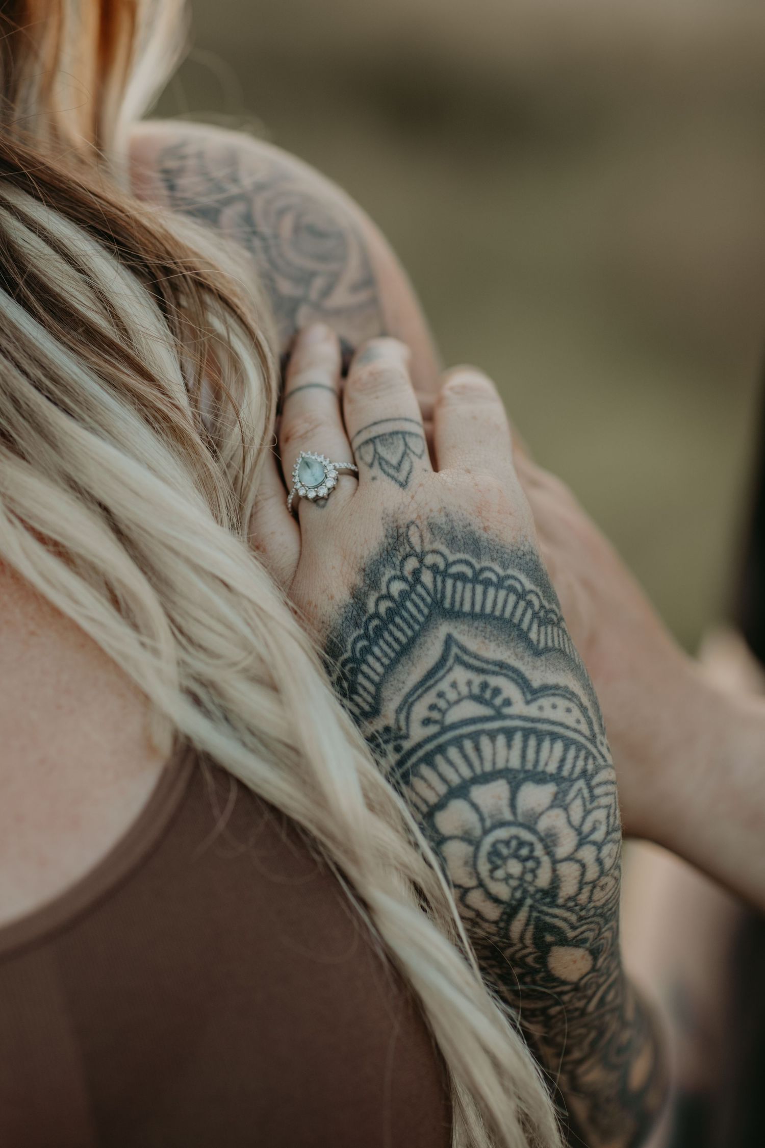 Close up of intricate mandala tattoo design and turquoise ring on woman's hand with blonde hair visible.
