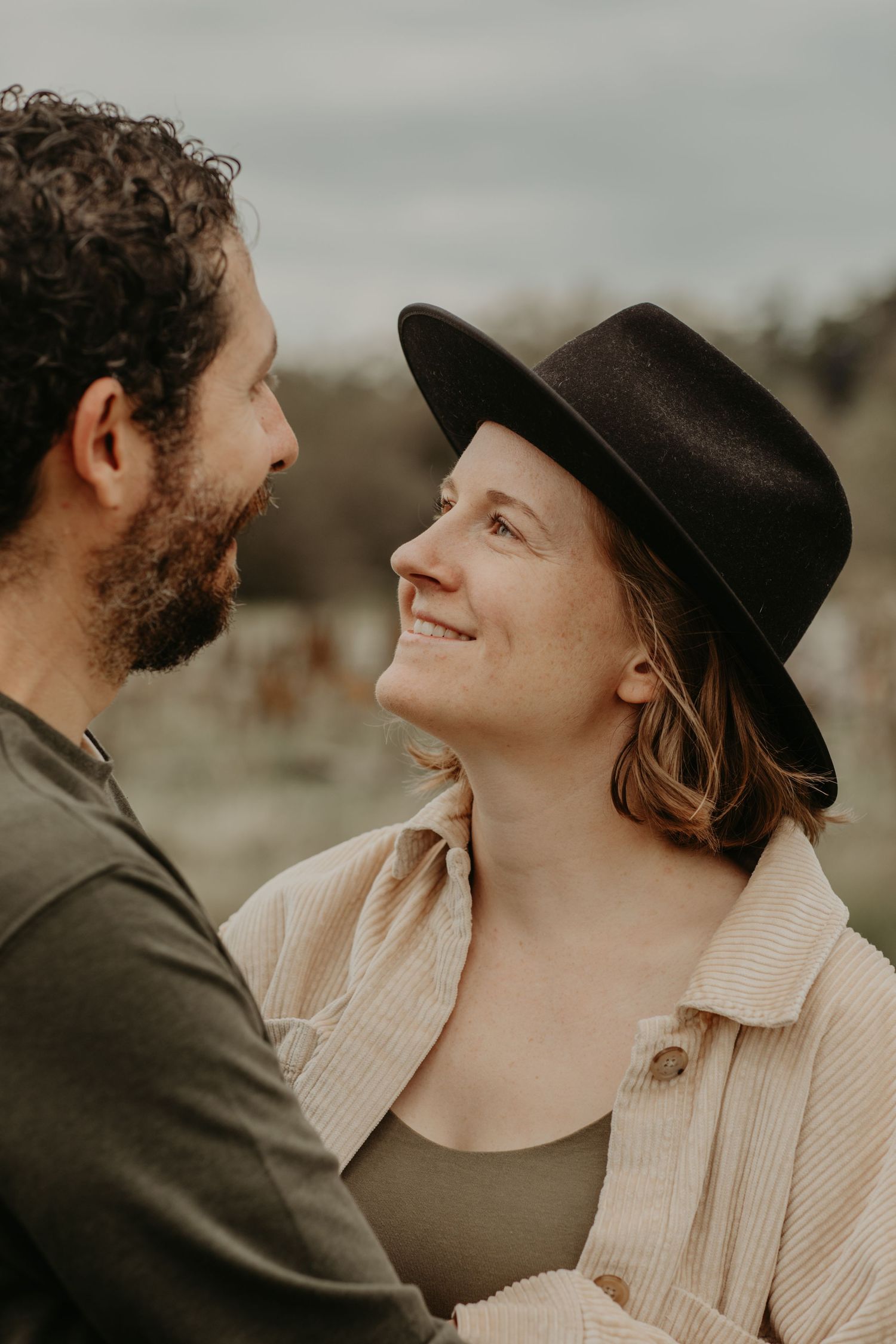 A candid romantic moment between a couple outdoors, with one wearing a black hat and cream cardigan at sunset.