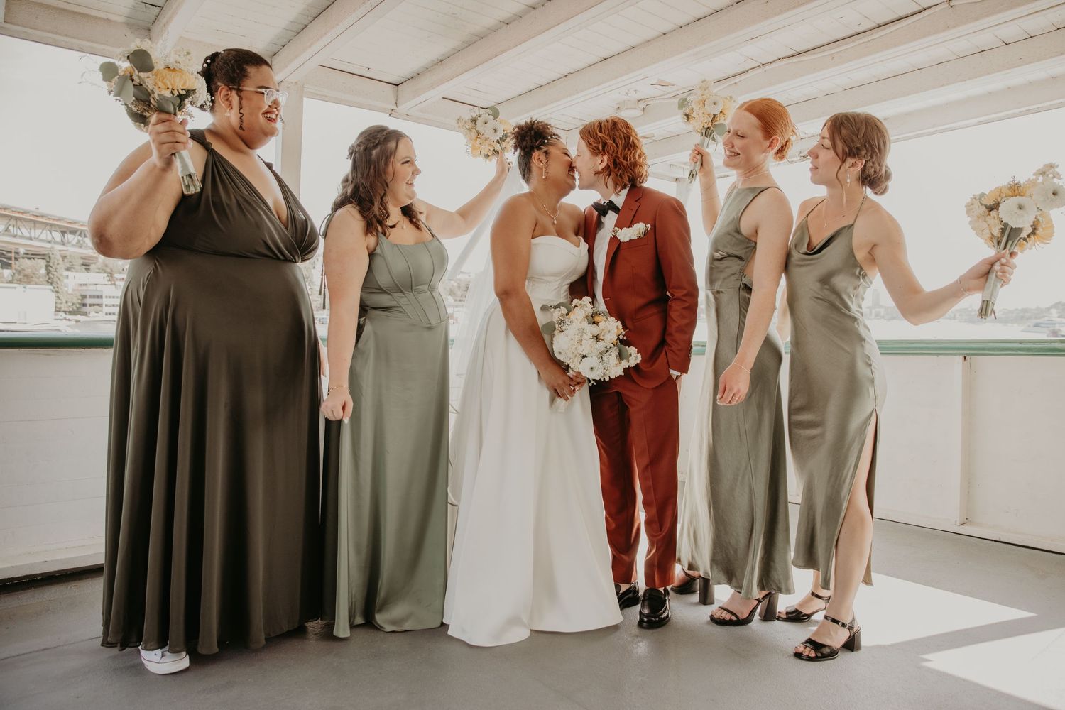 Wedding party in earth-toned dresses and suits standing together in a bright indoor space.