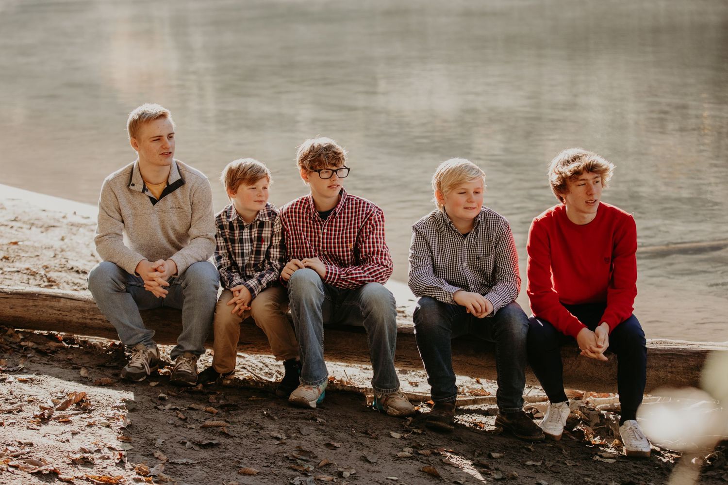 A group of people sitting together on a log by the water's edge during a cloudy day.