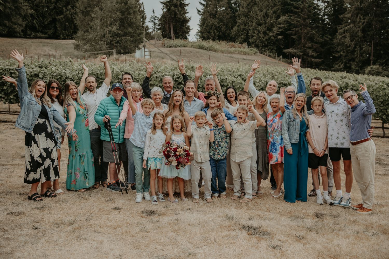 Wedding party and guests gather outdoors in coordinated teal and neutral colored attire for group photos.