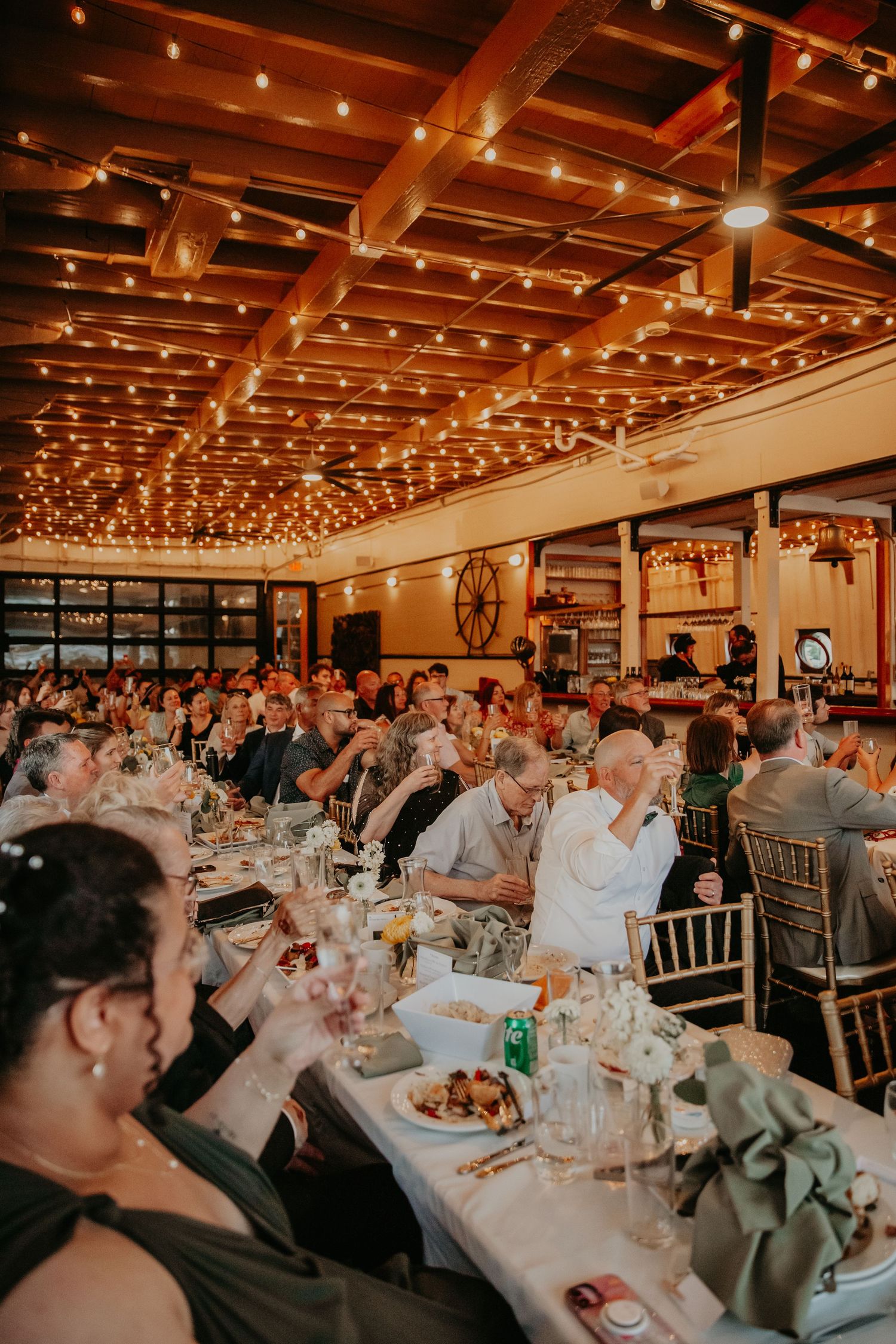 Wedding reception venue with string lights overhead and tables filled with guests enjoying dinner.