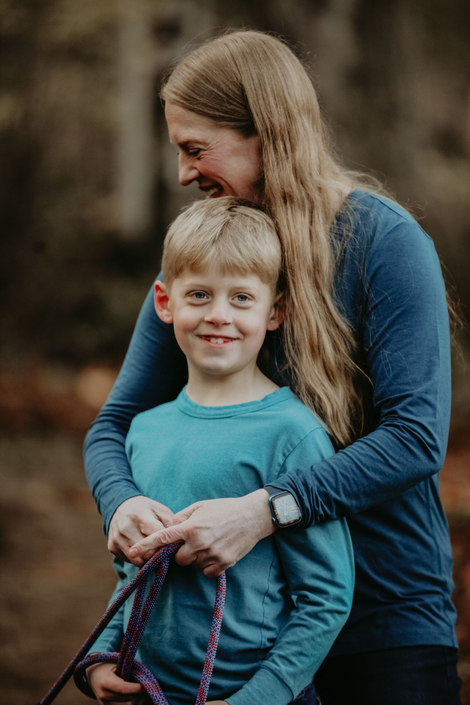A parent and child share a joyful moment outdoors wearing coordinating blue shirts on an autumn day.