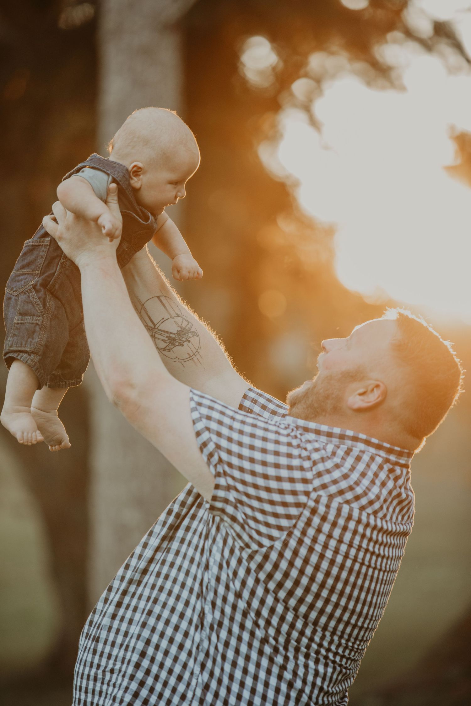 Parent lifting child in air against golden sunset creating silhouette effect in gingham pattern shirt.