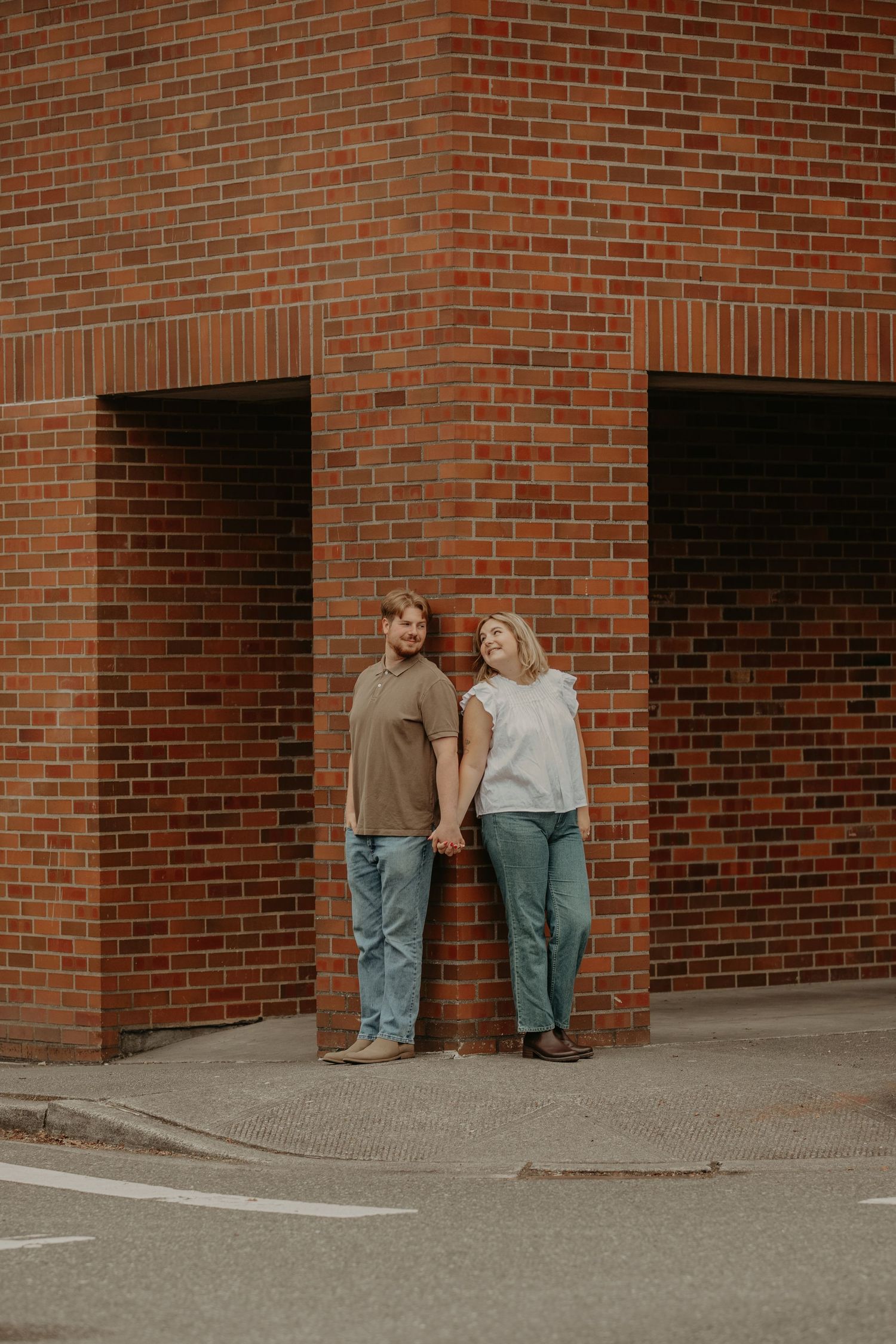 A couple poses together against a red brick wall with architectural details in the background.