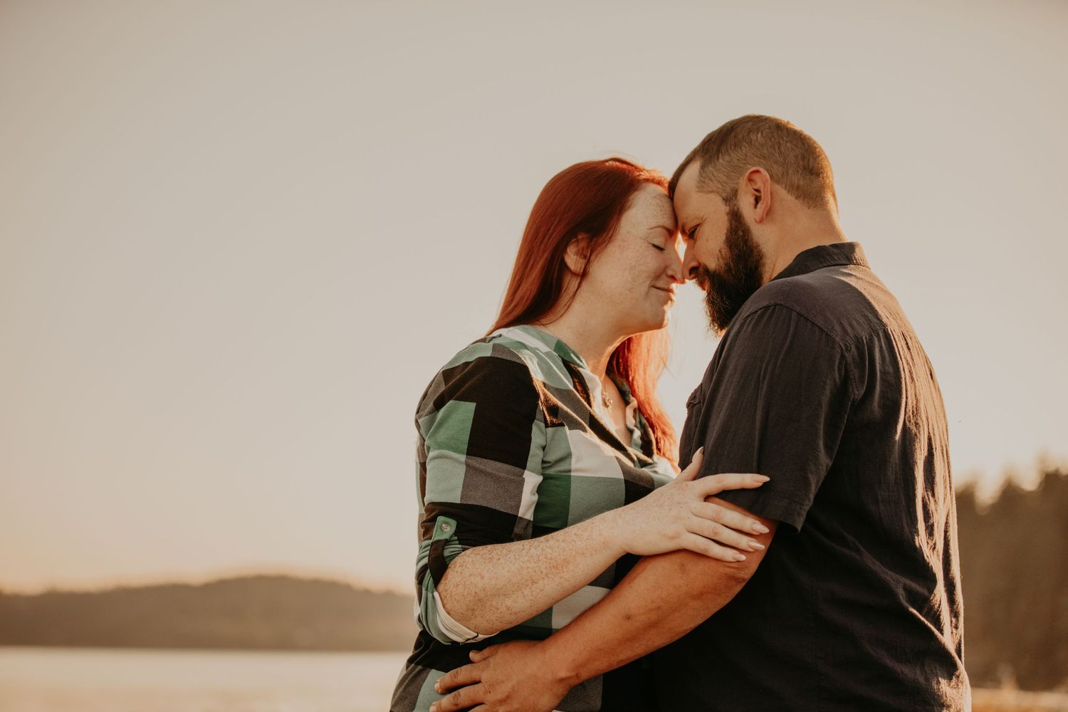 Intimate couple sharing a tender moment together at sunset by a lake in warm golden light.