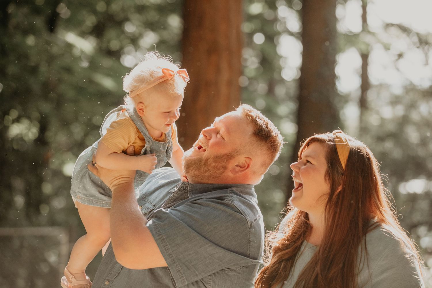 A family sharing a joyful moment together outdoors in warm sunlight among tall trees.