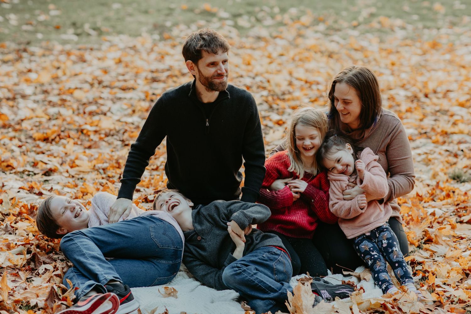Family sitting together on a blanket in autumn leaves during an outdoor fall photoshoot.