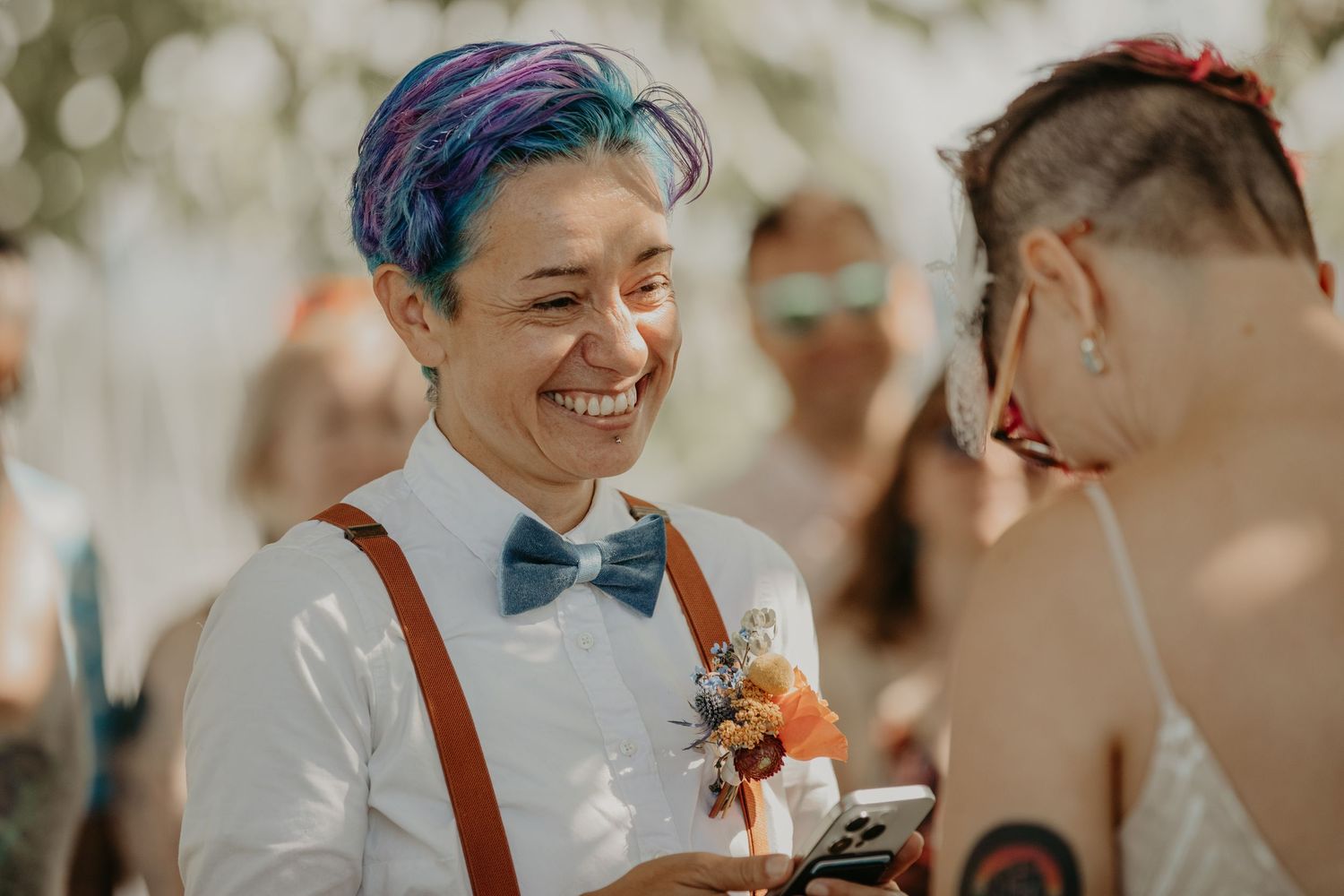 A joyful wedding celebration outdoors with guests sharing laughter and warm moments in natural lighting.