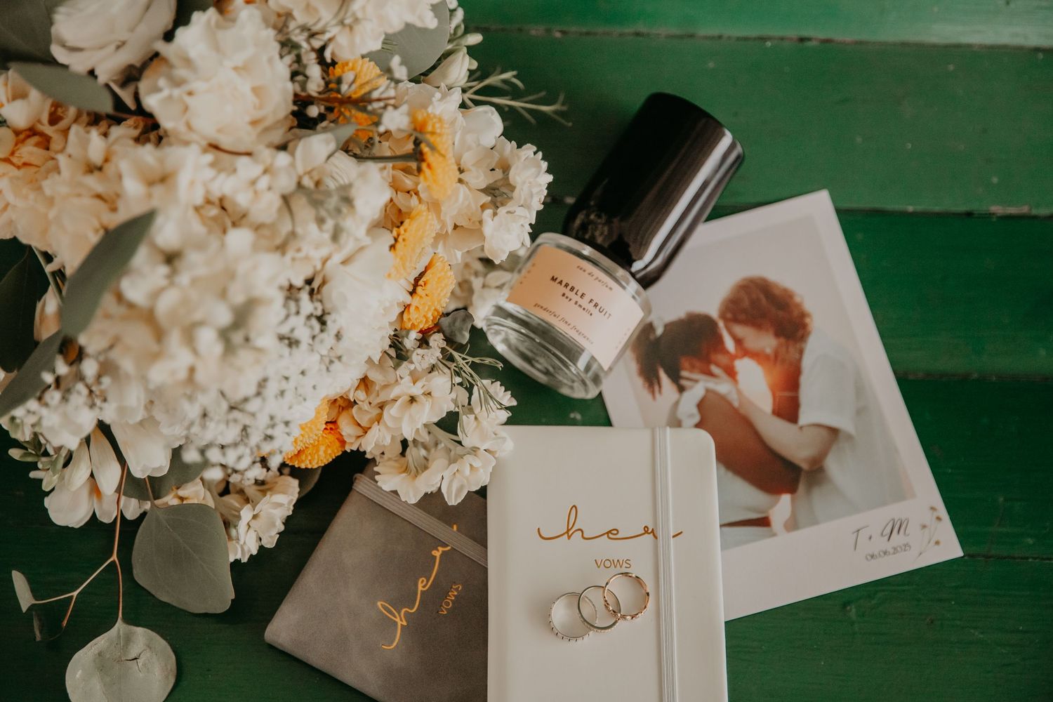 White hydrangea flowers and wedding stationery with calligraphy arranged on a green wooden surface.