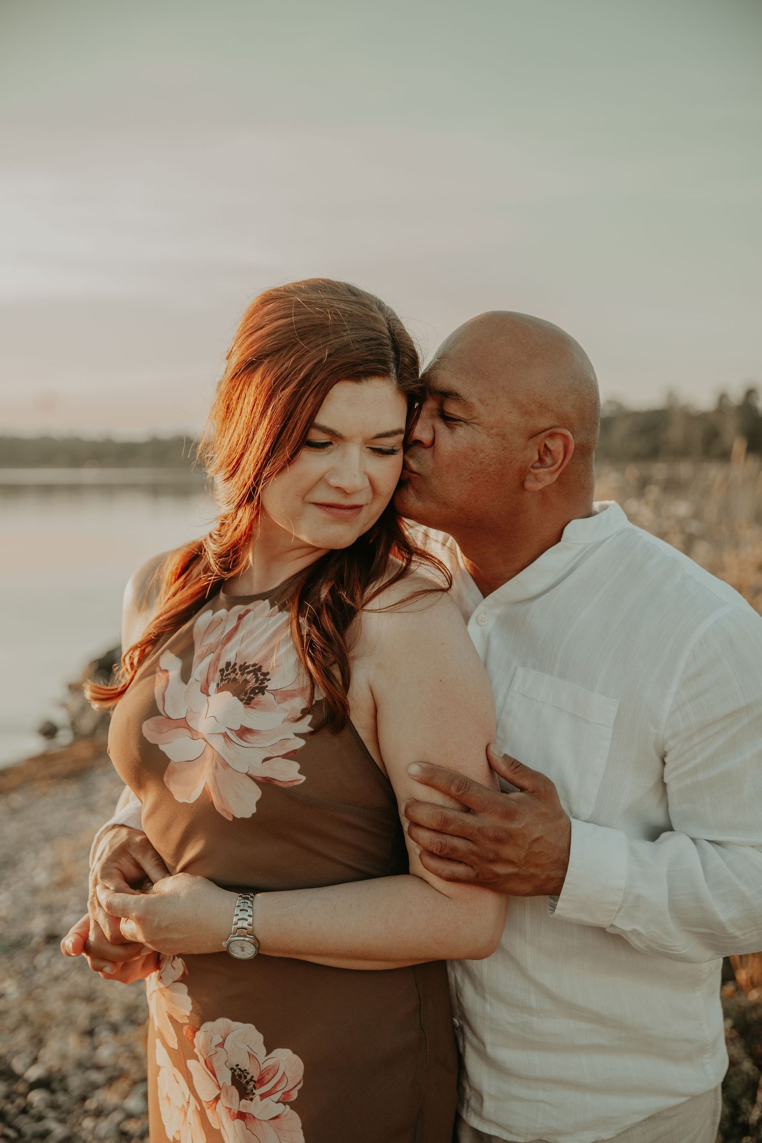 Intimate sunset portrait of couple embracing on a beach with warm lighting and ocean view.
