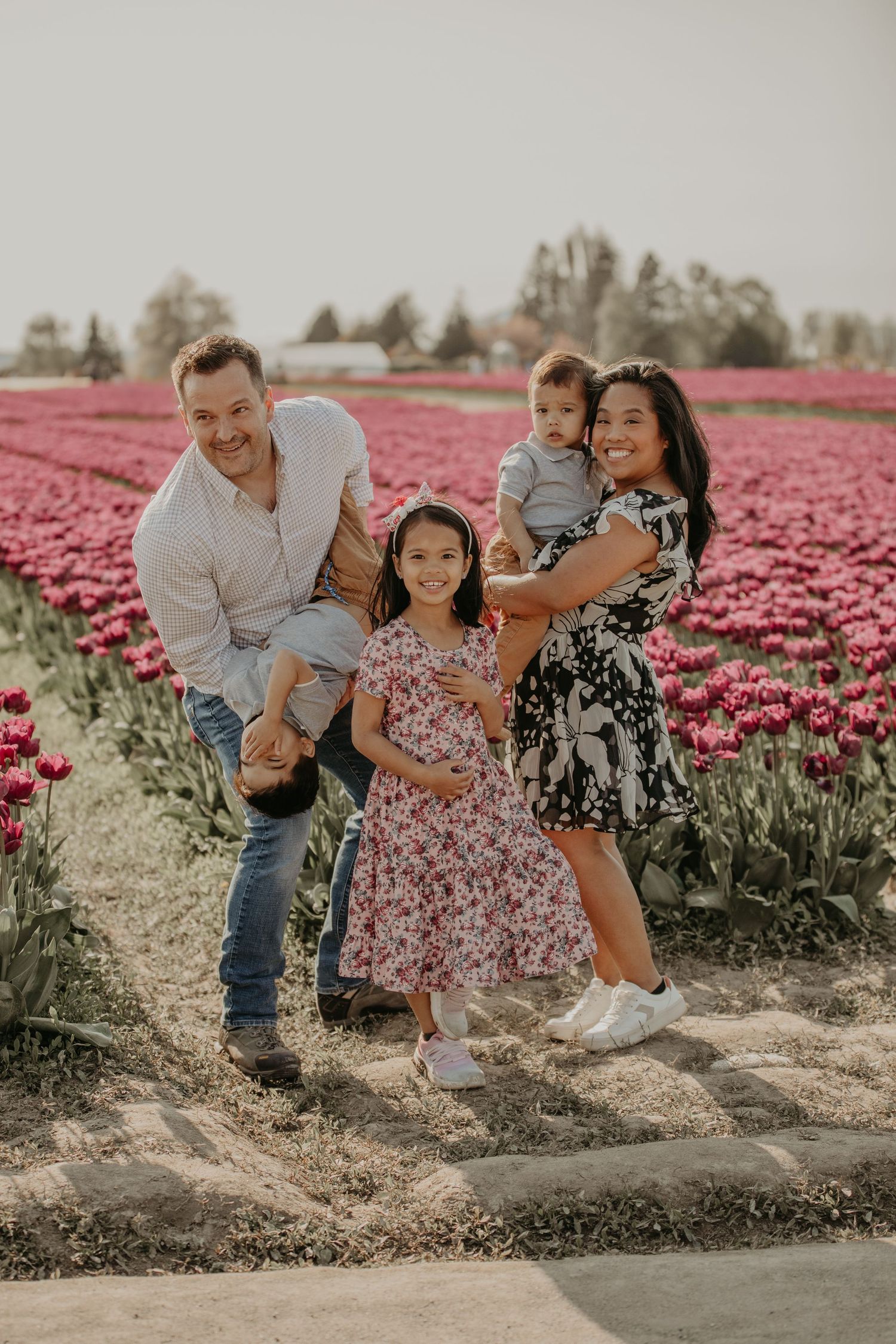 A family shares a joyful moment together in a vibrant field of pink tulips on a sunny day.