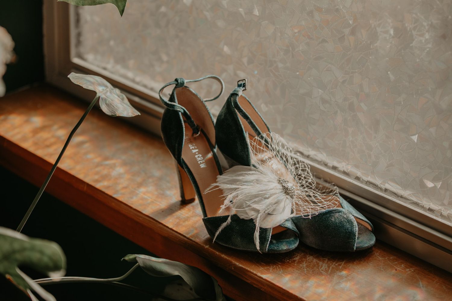 A white wedding dress hangs elegantly by a window, with soft natural light illuminating its delicate details.