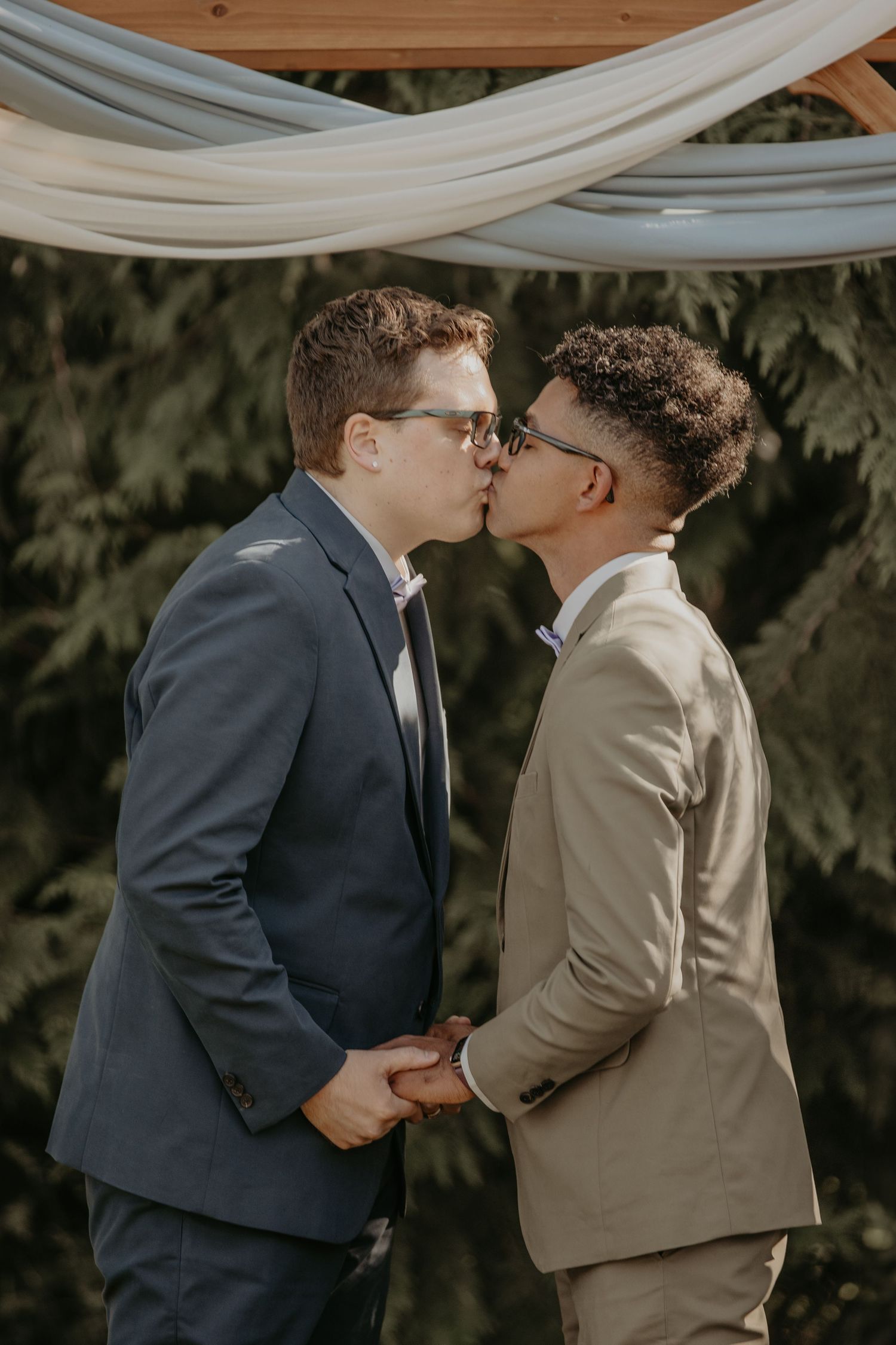 A tender moment shared under white fabric draping during a romantic outdoor celebration.
