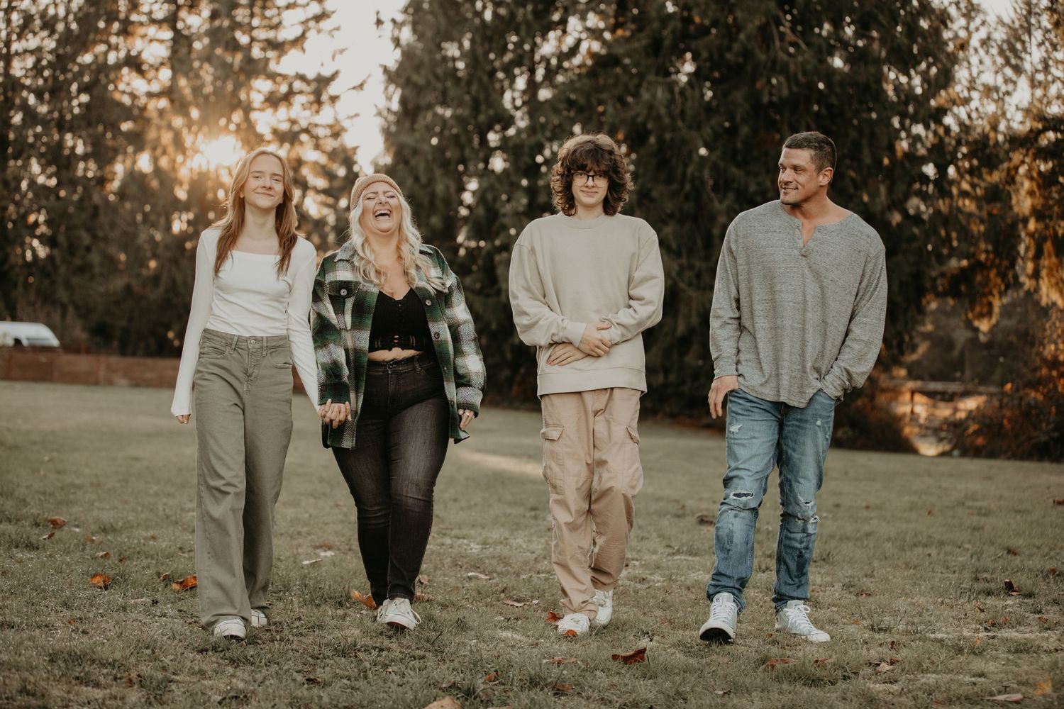 Four friends walk together on grass during golden hour sunset with trees in background.