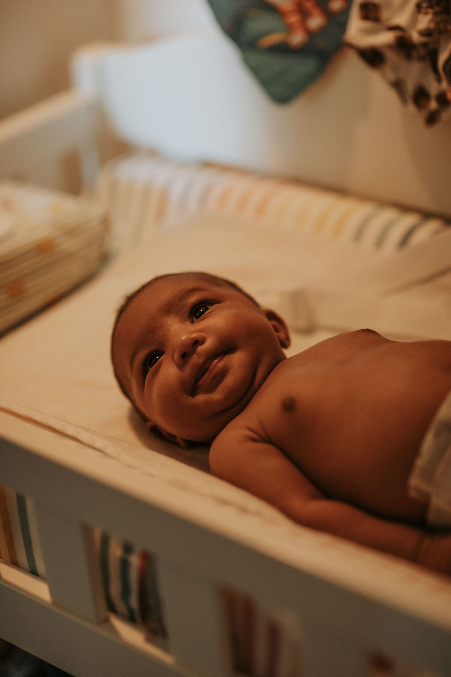 A happy baby lies in a white crib looking up with bright eyes and a joyful expression.