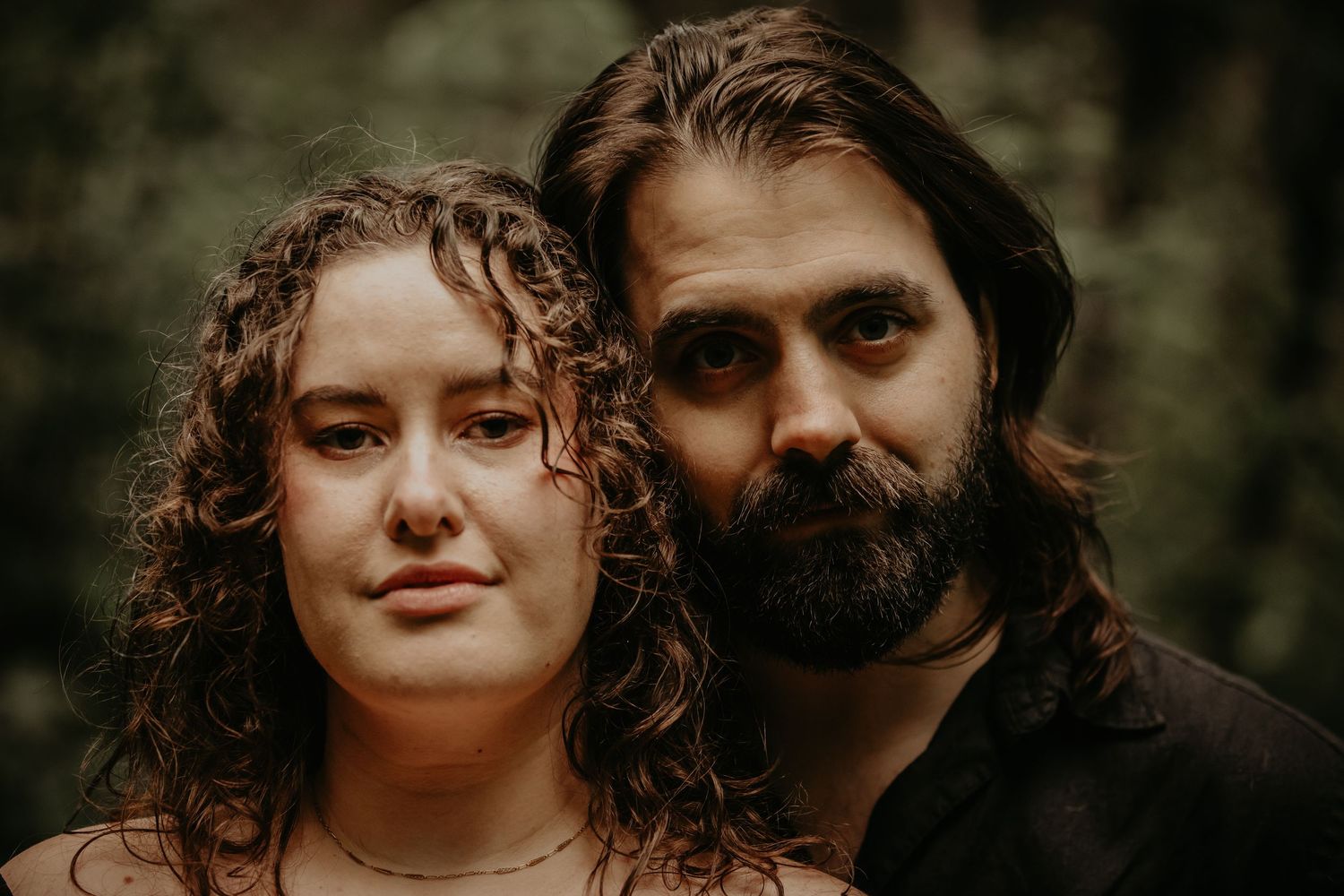 Close-up portrait of couple with rustic forest backdrop during engagement session.