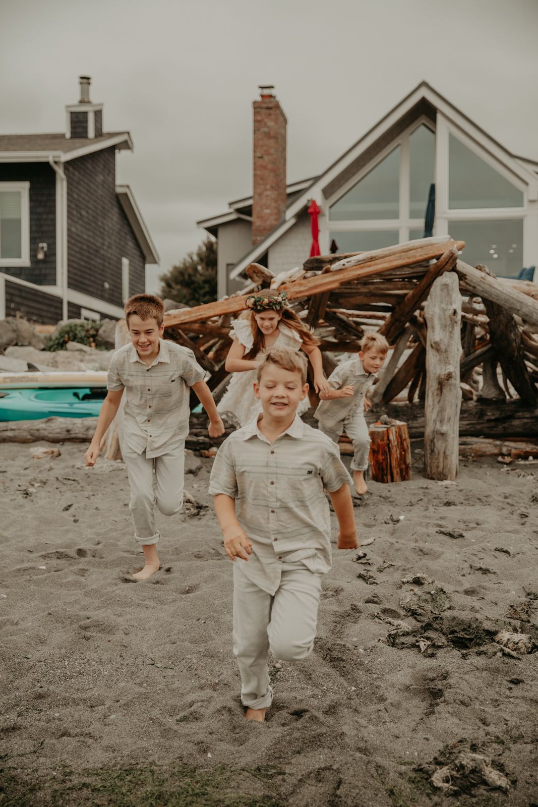 Two children run and play together on a sandy beach with houses visible in the background.