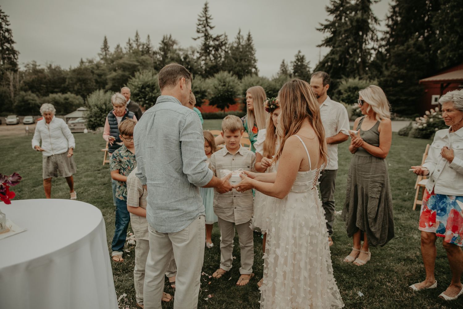 Wedding guests dance and celebrate outdoors among evergreen trees at a summer reception.