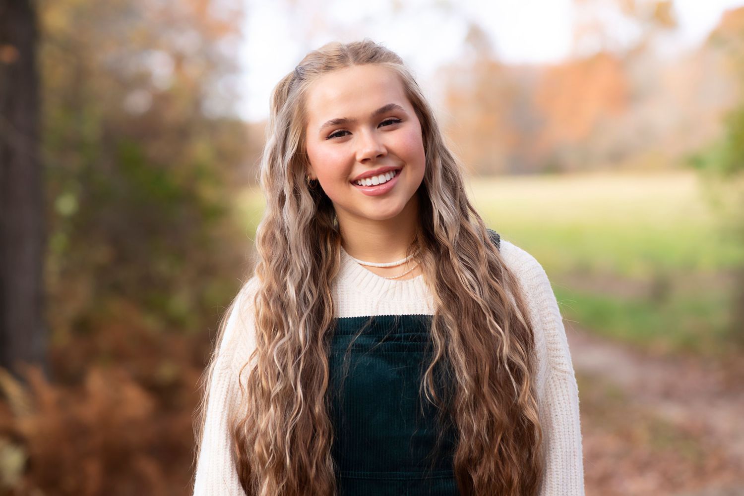 Outdoor fall portrait of someone wearing a green velvet overall dress and cream sweater with long wavy hair. Rhode Island Photographer