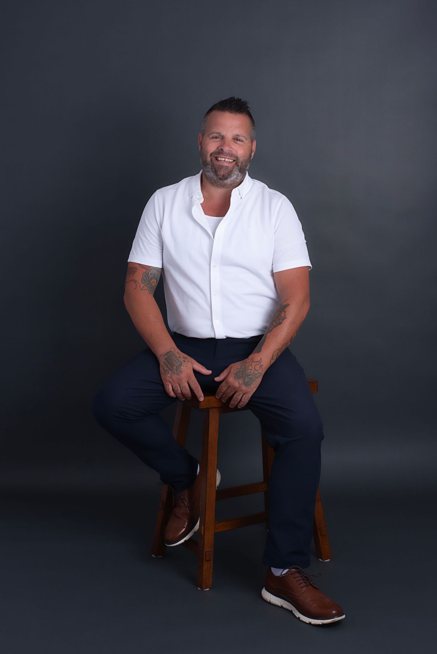 Studio portrait series showing someone in casual white t-shirt and navy pants seated on wooden stool against dark backdrop.