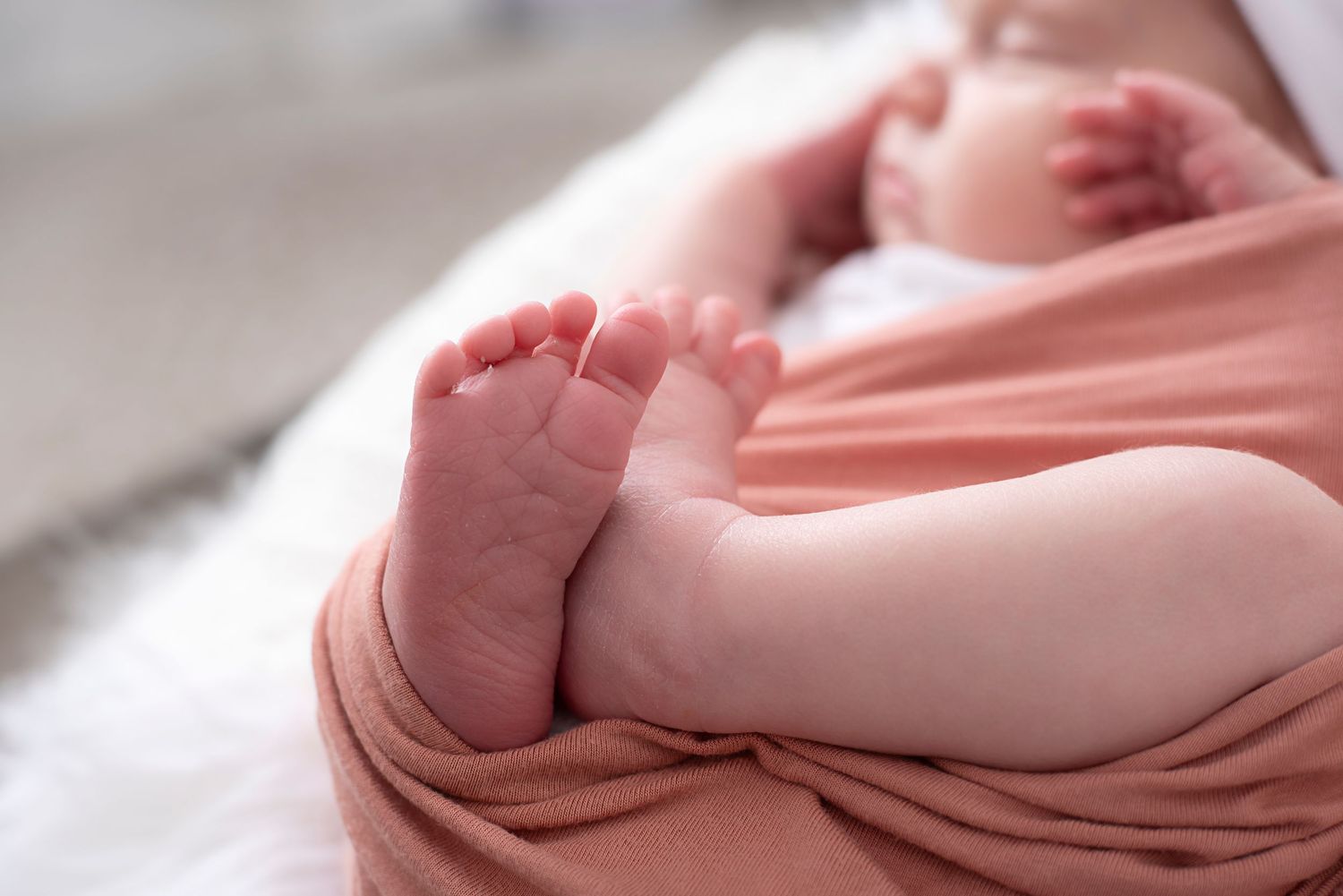 Close up of tiny baby feet wrapped in soft pink blanket showing delicate toes and skin.