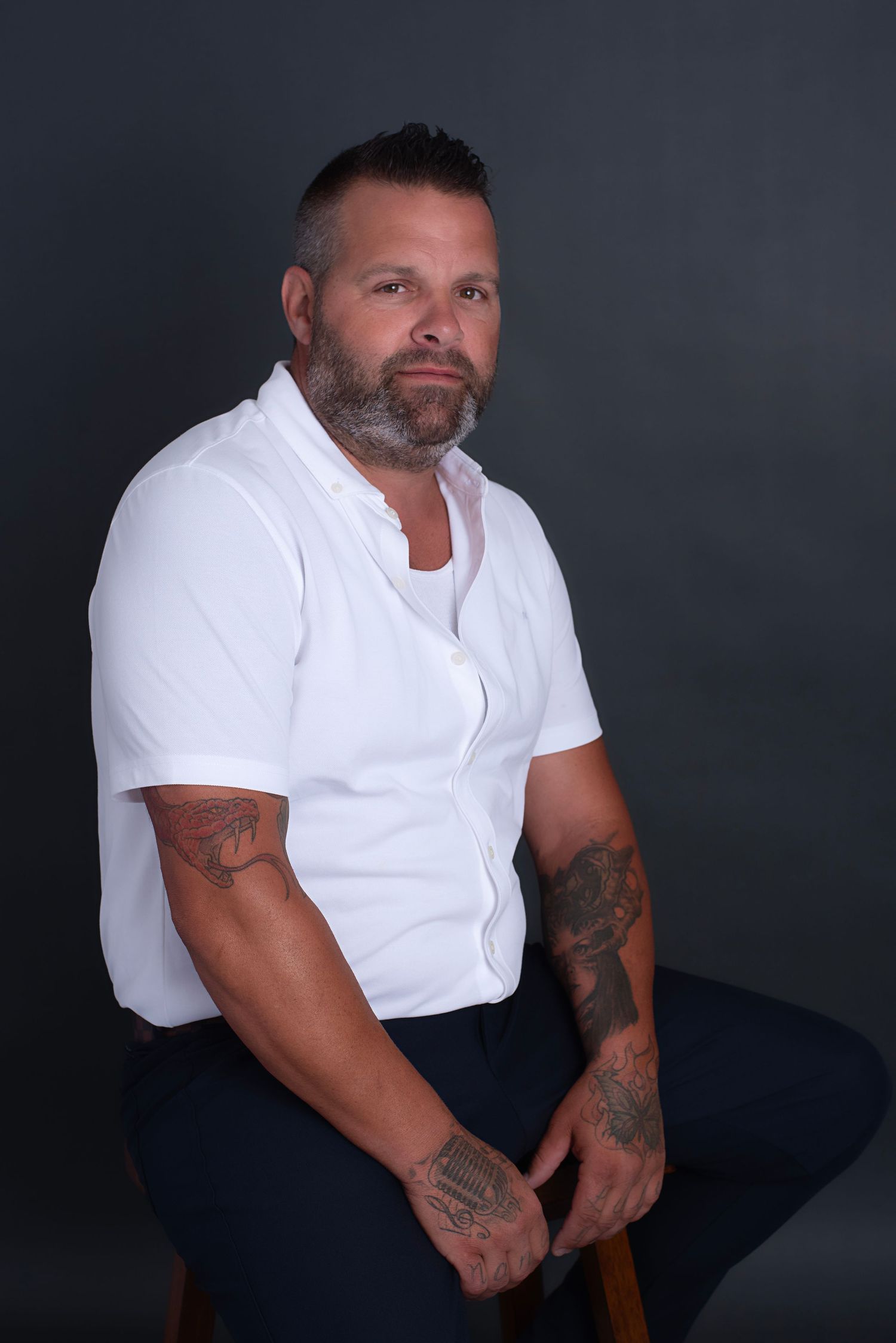 Studio portrait series of person in white t-shirt against dark background showing different seated poses with tattoos.
