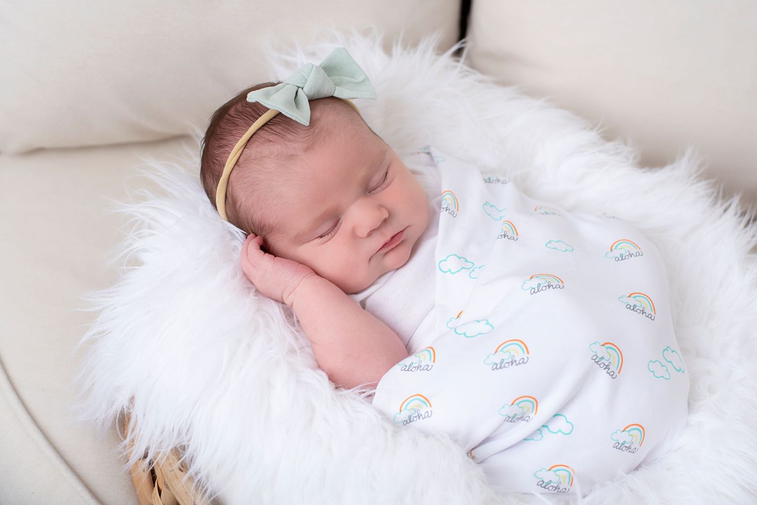 A delicate angel wing decoration adorns a sleeping newborn baby wrapped in soft white blankets during a photoshoot.